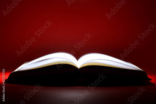 A book that looks like a Bible open in dark and red color background with very bright golden light on the page. Spiritual Life concept.