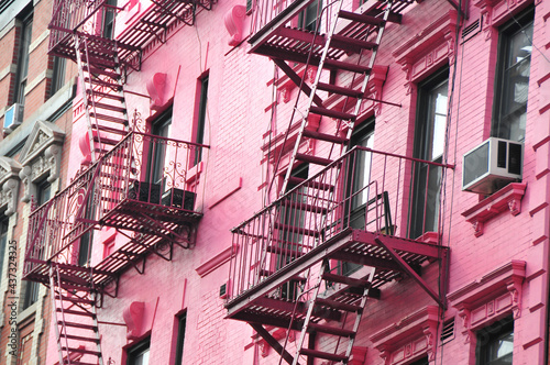 Fire escapes on the outside of an urban pink building in the middle of the Village in New York City