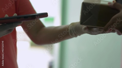 Close up of girl's hand receive a parcel from a delivery woman and using QR code scan with smartphone for payment. Scanning and paying on mobile device. Delivery to home concept.