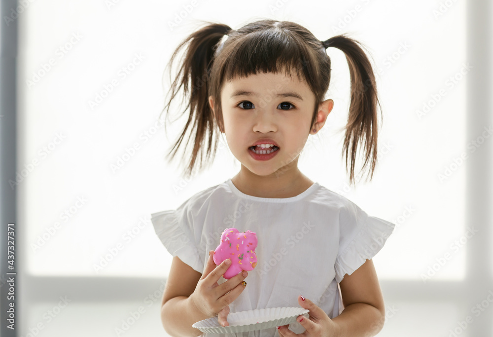 Portrait closeup shot of Asian sweet little cute happy cheerful kindergarten girl with bunches hairstyle standing look at camera holding paper dish and eating delicious strawberry flavor icing bread