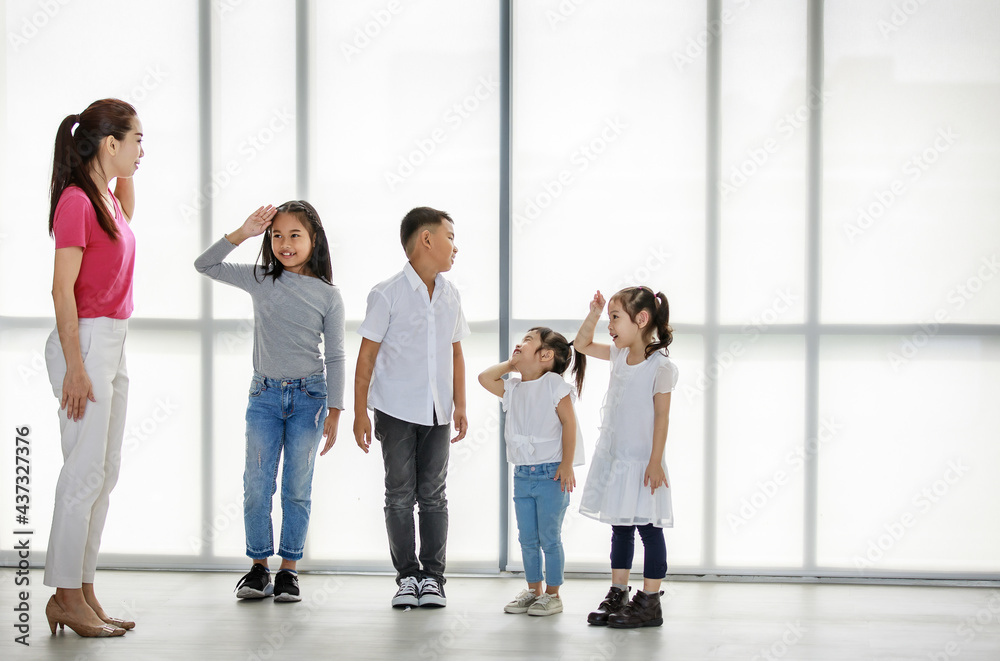 Asian female acting dancing activity class teacher teaching group of naughty little boy and girls students in pre-elementary school to standing holding hand up to salute in private classroom studio Asian female acting dancing activity class teacher teaching group of naughty little boy and girls students in pre-elementary school to standing holding hand up to salute in private classroom studio