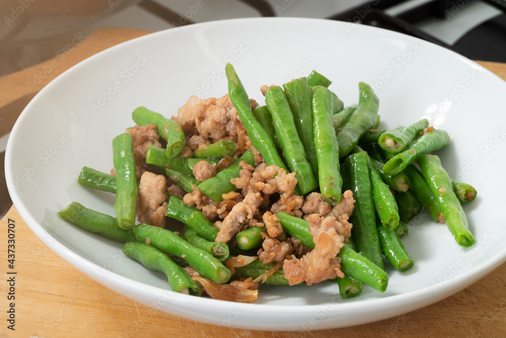 Close up stir-fried cowpeas or black-eyed beans with minced pork with garlic and soy sauce, food in the white disk on cutting board in the kitchen, Asian homemade menu.