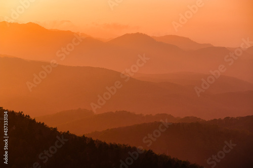 Layered silhouettes of hills and bright orange sunset during sand storm