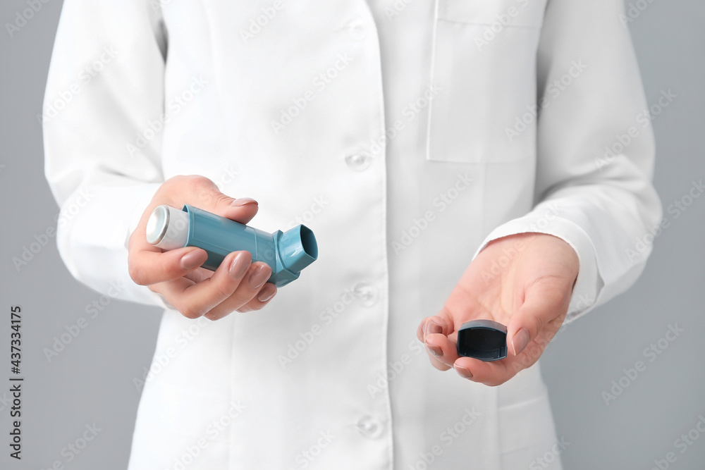 Female allergist with inhaler on grey background Female allergist with inhaler on grey background