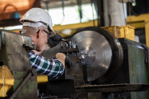 worker is working on a lathe machine in a factory. Turner worker manages the metalworking process of mechanical cutting on a lathe photo