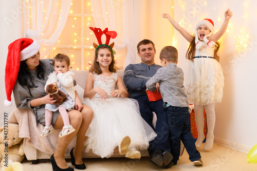 happy big family portrait - parents and children in home interior decorated with holiday lights and gifts, dressed in santa hat for new year celebration