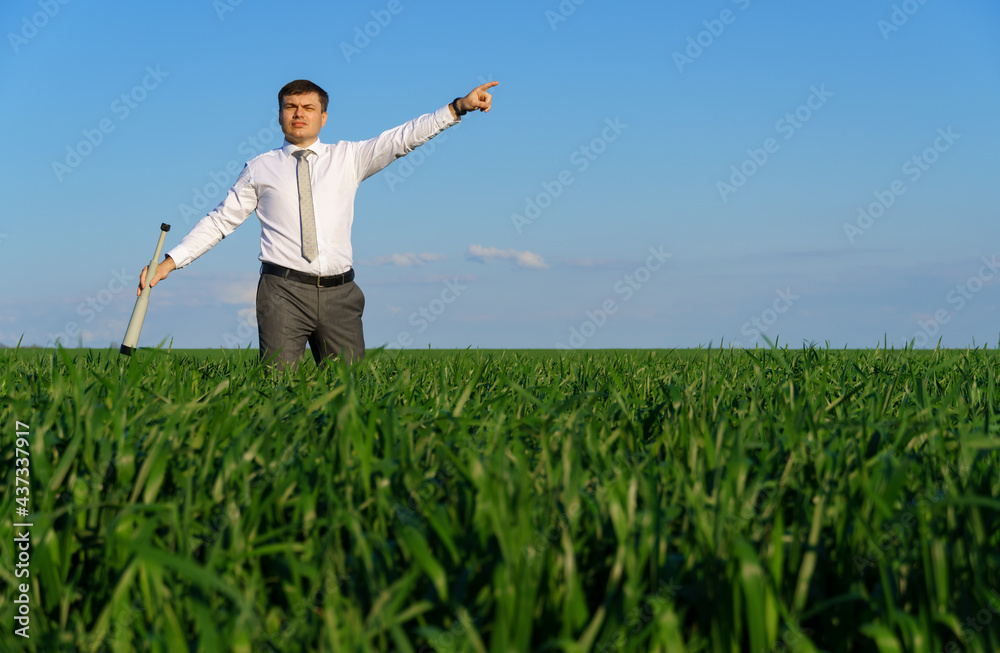 businessman poses with a spyglass, he looks into the distance and looks for something, green grass and blue sky as background