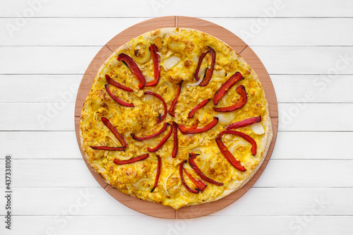 Whole round pizza topped with red pepper, onion and yellow curry sauce on wooden plate. Top view on white board background with copy space.