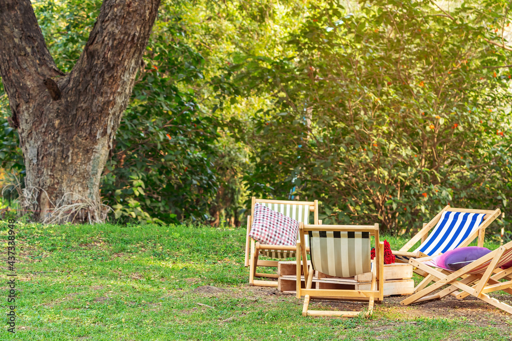 Many deck chairs and pillows with wooden table in the courtyard is surrounded by shady green grass. Comfortable pillows on outdoor patio chair and table in garden. Summer vacation. Selective focus. Many deck chairs and pillows with wooden table in the courtyard is surrounded by shady green grass. Comfortable pillows on outdoor patio chair and table in garden. Summer vacation. Selective focus.
