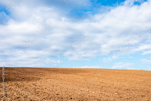 Plowed brown field and white clouds on blue sky.cloudy sky over brown field.Spring summer day.