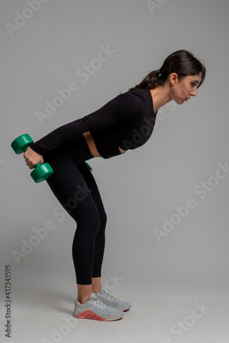 Foto Sporty girl performing triceps kickback with dumbbells on grey background