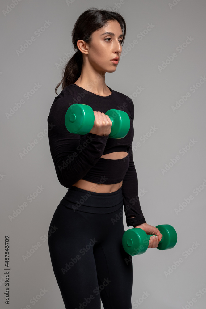 Athletic girl performing dumbbell bicep curl on grey background Athletic girl performing dumbbell bicep curl on grey background