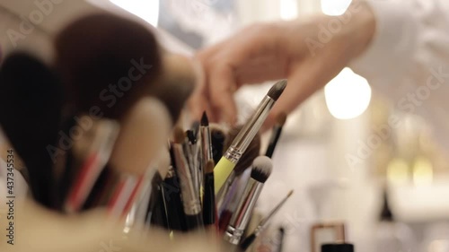 Crop makeup artist choosing brush. Unrecognizable female professional visagiste picking applicator from collection placed on table in beauty studio 