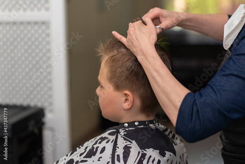 Cutting hair for young boy in a beauty salon.Hairdresser's hands holding a comb and a colorful scissors.Closeup.