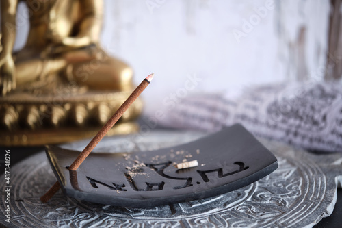 Tibetische Räucherstäbchen auf schwarzem Specksteinhalter mit goldenem Buddha (Close-up) photo