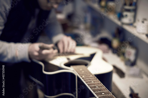 A service worker repairs a guitar with a tool.