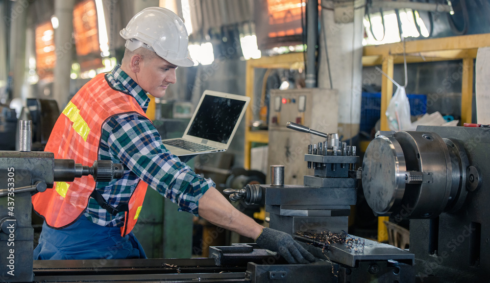 man Lathe worker in production plant drilling at machine on the factory. Industrial engineer worker holding laptop Inspect workpieces