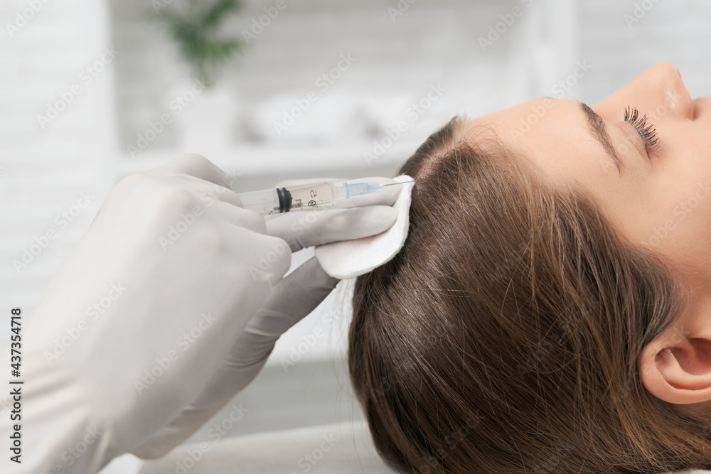 Side view of young brunette woman on procedure for improvements hair condition with special cosmetics. Concept of different procedure for hair restoration in professional beauty salon. 