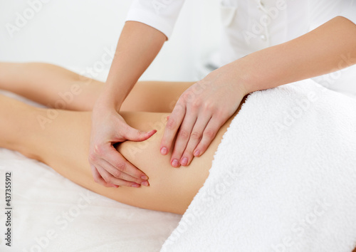 Therapist doing anti cellulite massage on legs for female client lying at beauty center or spa salon photo
