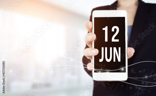 June 12nd. Day 12 of month, Calendar date. White smartphone with Calendar date in businesswoman hand on blurred background. Summer month, day of the year concept.