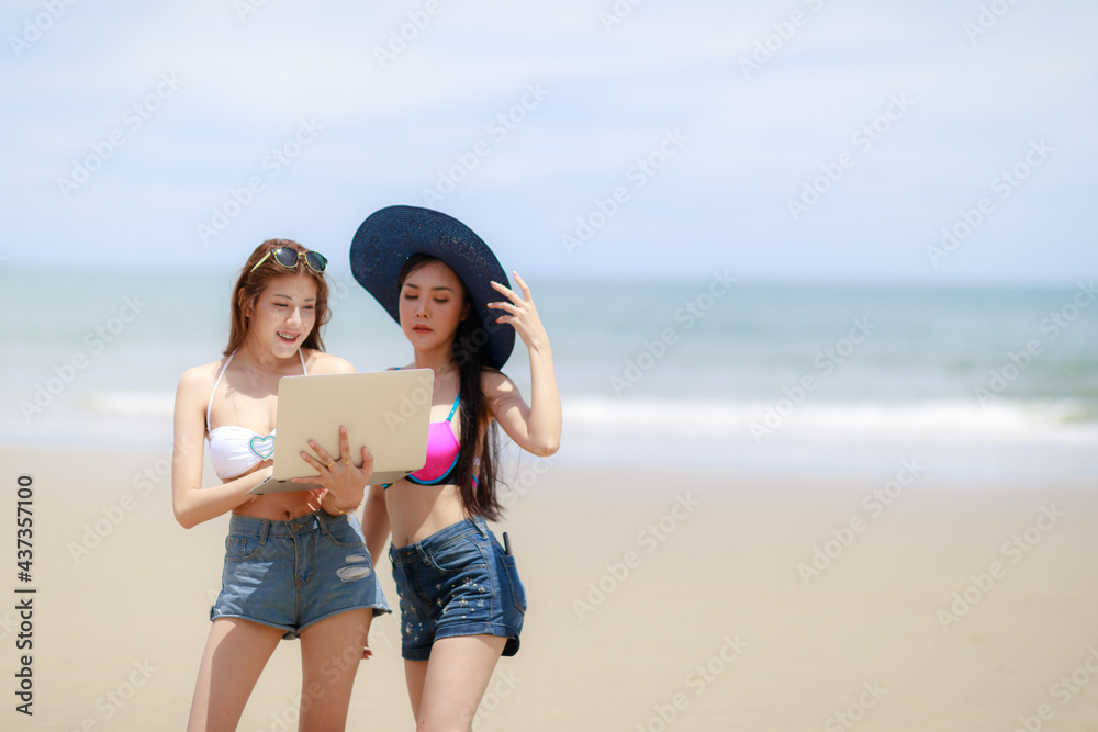 Two sexy Asian woman with the notebook pc relaxing on the beach Two sexy Asian woman with the notebook pc relaxing on the beach
