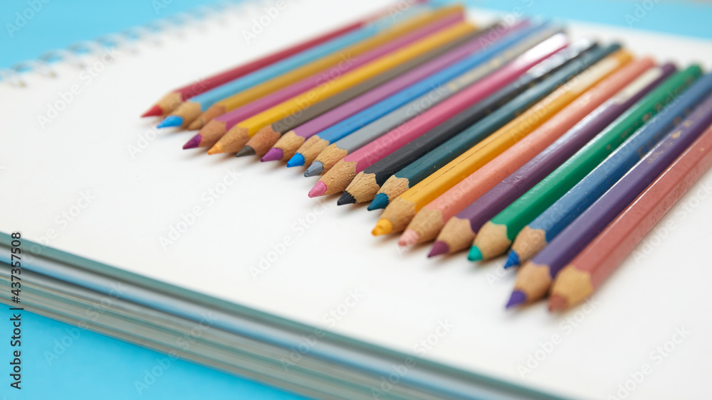 Colorful pencil crayons on a notebook on blue background Colorful pencil crayons on a notebook on blue background