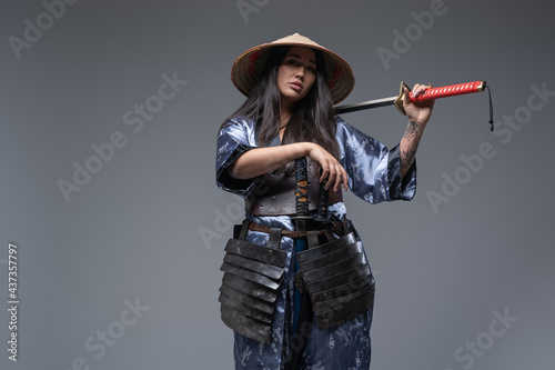 Japanese female killer with katana posing against gray background