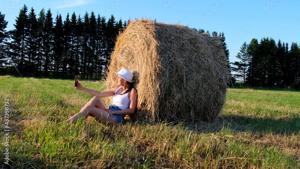 young female makes a selfie on a smartphone near a haystack and talks on video communication. Rural area. freedom concept young female makes a selfie on a smartphone near a haystack and talks on video communication. Rural area. freedom concept
