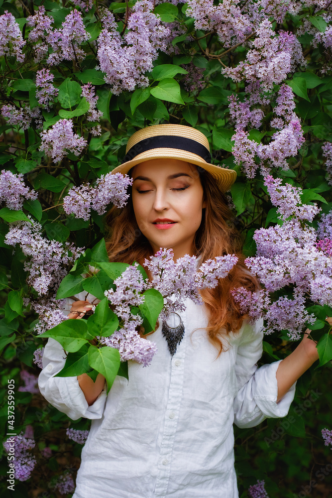 Portrait of a young beautiful woman in a straw hat near a blooming lilac bush. The girl closed her eyes dreamily. Copy, empty space for the text. Vertical.