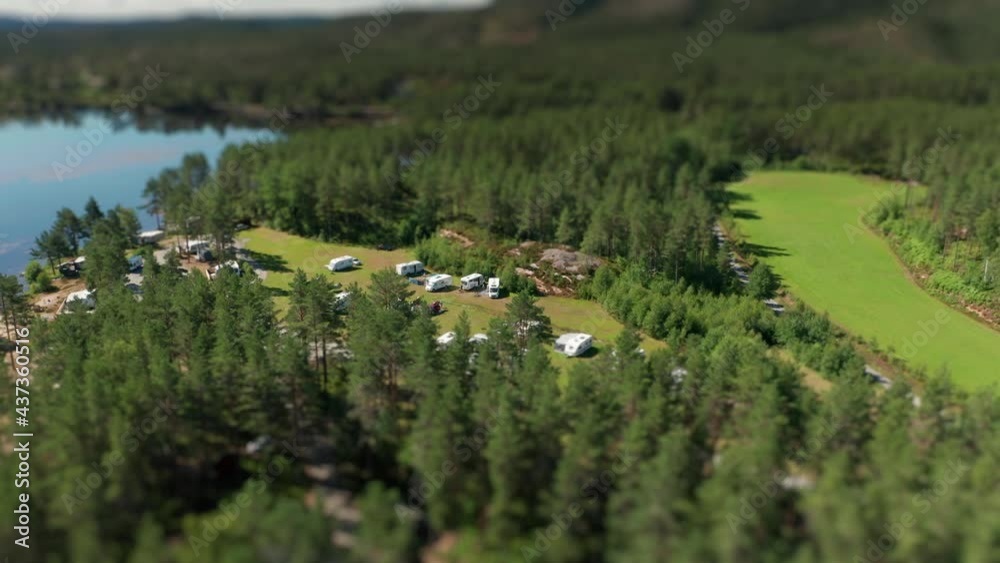 Camping cozily tucked in between the trees and on the bank of the Otra river. Campers, caravans, cars, and tents scattered on the grass. Cabins hidden under the tall pine trees. A tilt-shift video. Camping cozily tucked in between the trees and on the bank of the Otra river. Campers, caravans, cars, and tents scattered on the grass. Cabins hidden under the tall pine trees. A tilt-shift video.