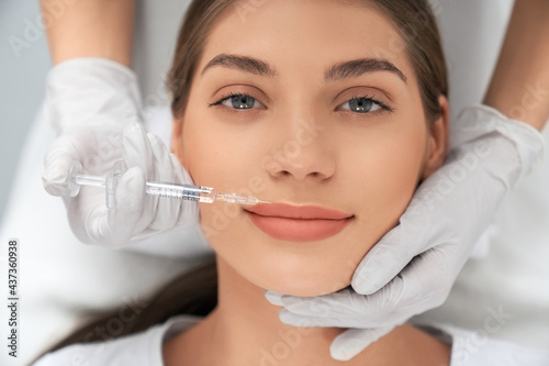 Fototapeta Naklejka Na Ścianę i Meble -  Top view portrait of smiling attractive young brunette woman on procedure for augmentation lips in professional beautician. Concept of beauty procedure for improvements lips in salon. 