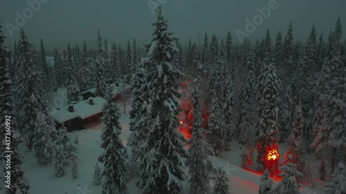 Aerial view of a snowy trees and cottages in Lapland, winter evening - tracking, drone shot photo