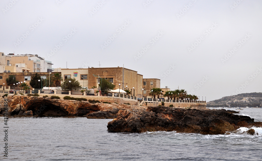 Photo of the buildings, the promenade and the rocky shore of Buggiba, Malta, Europe. Picture taken by boat.