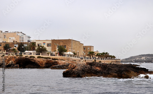 Photo of the buildings, the promenade and the rocky shore of Buggiba, Malta, Europe. Picture taken by boat.