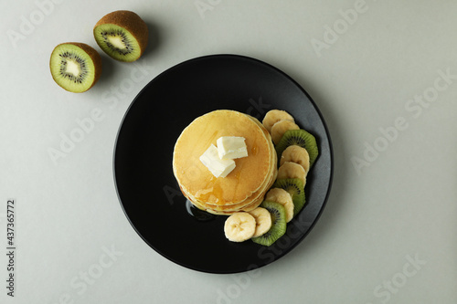 Plate with delicious pancakes and kiwi on gray background