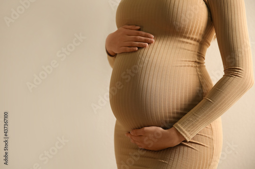 Pregnant woman touching her belly on beige background, closeup. Space for text