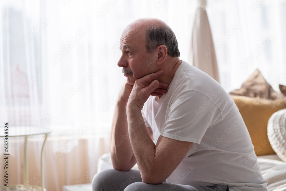 Sad senior man with head in hands sitting on bed at home