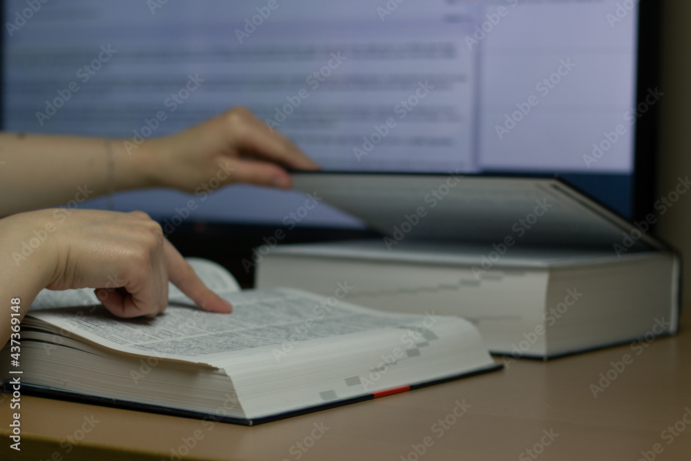 Closeup of a translator working with CAT (Computer-Assisted Translation) tool and dictionary.