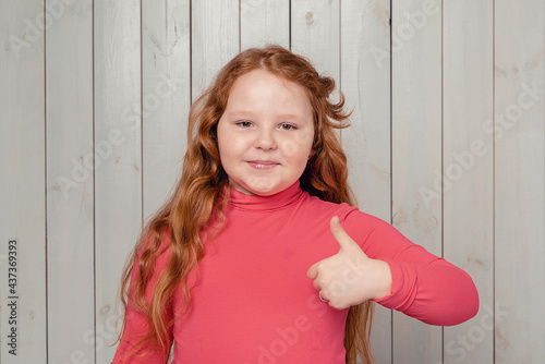 Cheerful redhead preteen girl shows thumb up and say yes, smiling satisfied, approve and like something good
