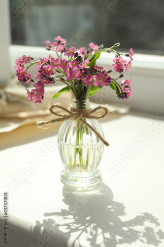 Beautiful pink forget-me-not flowers in glass bottle on window sill