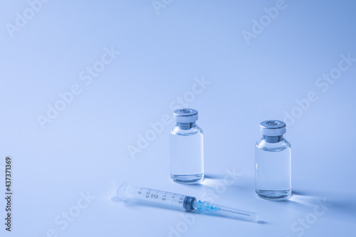 vials of medicine/vaccine and syringe against blue background