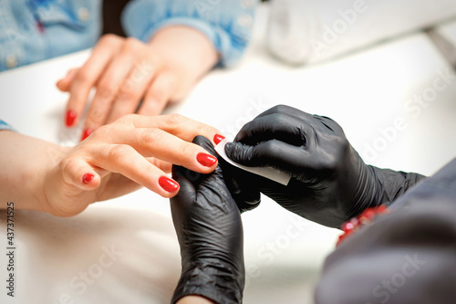 Closeup of manicure master in black gloves wiping the female red nails with a paper napkin in the beauty salon