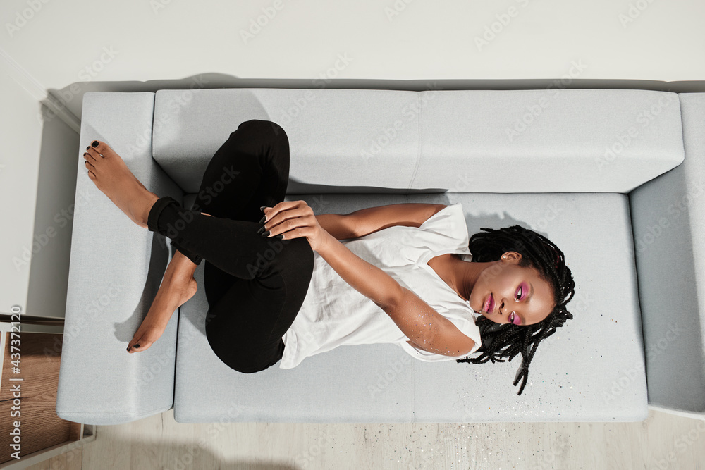 african american girl in white t-shirt and black jeans on the sofa ...