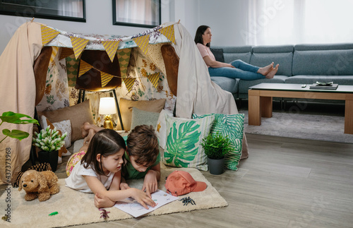 Children playing camping at home while their mother watches TV sitting on the sofa photo