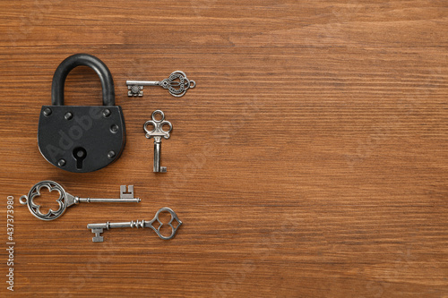 Padlock and beautiful vintage keys on wooden table, flat lay. Space for text