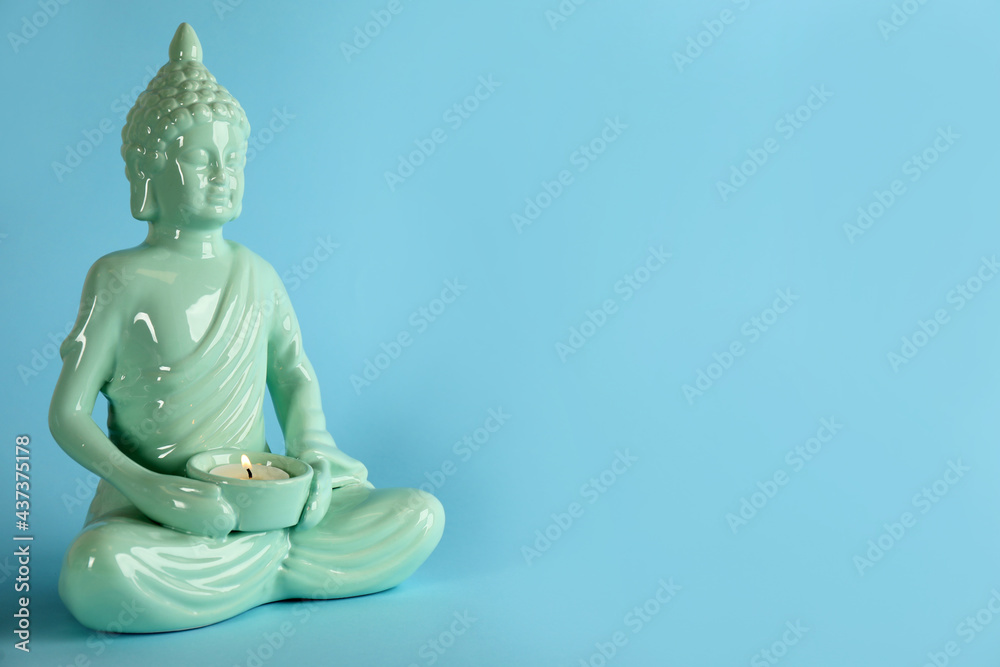 Beautiful ceramic Buddha sculpture with burning candle on light blue background. Space for text