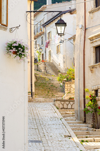 Pescocostanzo, Italy. August 24th, 2012. Alley with old style street lamp on the wall of a building and flowers in the windows in the old town.