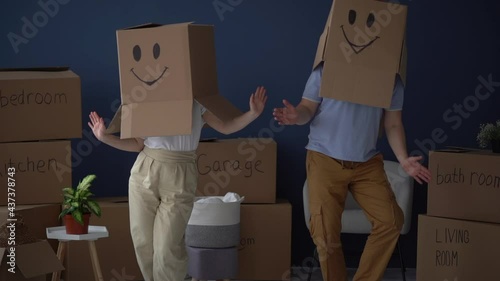 Unrecognizable couple, husband and wife, dancing with cardboard boxes on their heads, funny video. Moving and relocation concept. Packing and decluttering