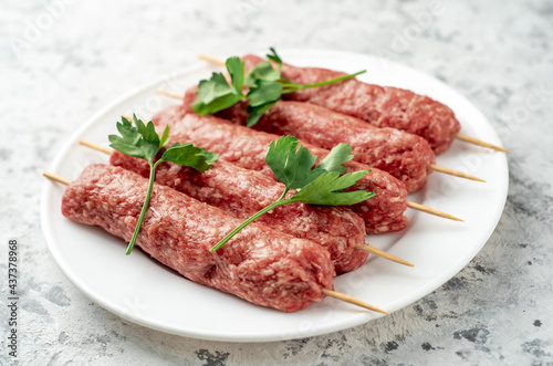 raw Lula kebab on skewers with spices on a white plate on a light stone background