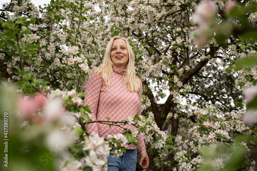 Blonde woman standing and posing in apple blossoms with dental braces, pink color